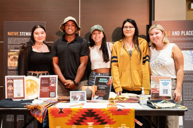 Five students pictured behind an information table for the student group Native at VT. Student members of Native@VT welcome Virginia Tech students both to campus and back to campus at the Cultural and Community Centers' open house Fall '22 kickoff event.